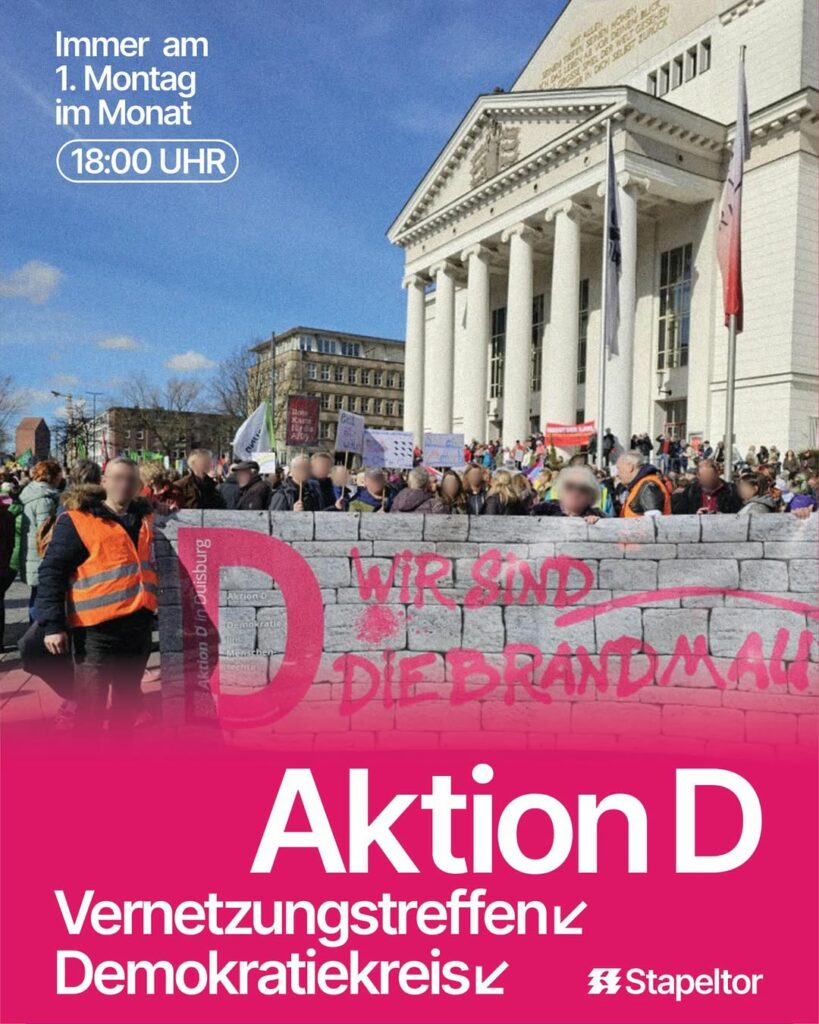 Demonstration vor einem historischen Gebäude mit Säulen, Banner mit Schrift 'Wir sind die Brandmauer', Veranstaltungshinweis 'Aktion D Vernetzungstreffen Demokratiekreis, immer am 1. Montag im Monat, 18:00 Uhr'