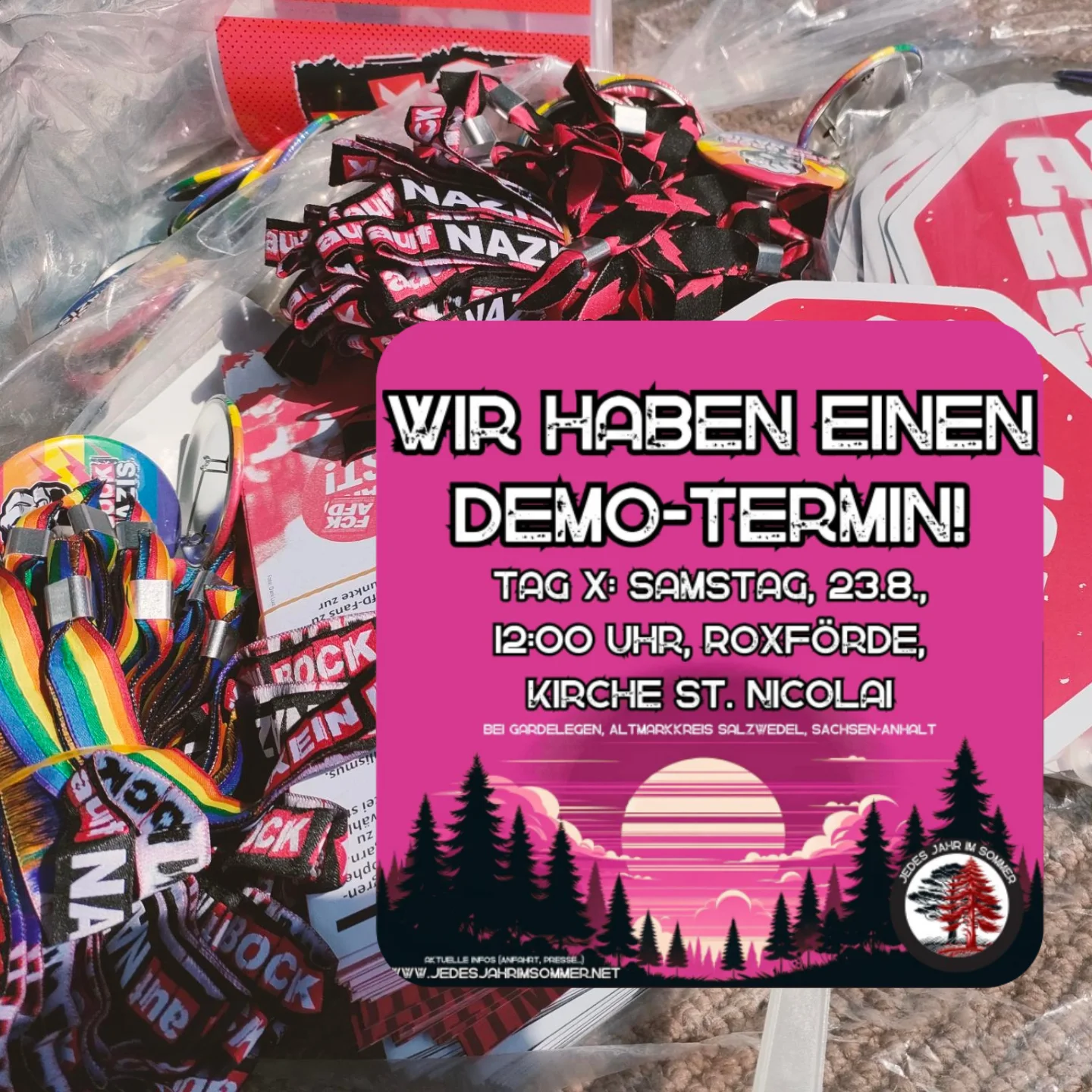 Plakat mit pinkem Hintergrund zeigt Sonnenuntergang hinter Tannenwald, Text 'Wir haben einen Demo-Termin! Tag X: Samstag, 23.8., 12:00 Uhr, Roxförde, Kirche St. Nicola', darunter Website und Logo mit Baum und Schrift 'Jedes Jahr im Sommer' Im Hintergrund des Plakats ein Bild von Schlüsselanhängern, Flyern und Aufklebern gegen Rechts.